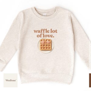 A cute, hand drawn waffle with heart toppings in soft colors - detailed view of a white baby bodysuit with product feature highlights - exclusive WeeBoss print detail