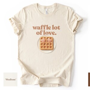 A cute, hand drawn waffle with heart toppings in soft colors - detailed view of a cozy natural heather toddler sweatshirt with product feature highlights - exclusive WeeBoss print detail