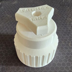 Könnte beinhalten: Eine weiße, 3D-gedruckte Kunststoffkomponente mit einem zylindrischen Sockel mit vertikalen Rillen und einem Oberteil mit einem sechseckigen Mittelloch. Das Oberteil ist mit dem Text TRI-HEX LINK in dreieckiger Anordnung geprägt.