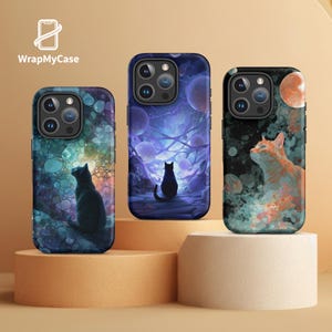 May include: Three phone cases with cat-themed art. The cases feature a black cat in a dreamlike setting, a black cat on a path, and an orange cat looking up at a moon. The cases are on a beige display.