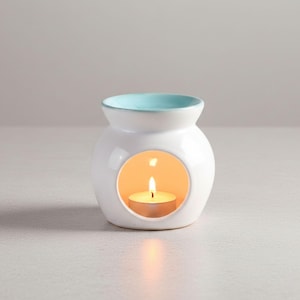 Pode incluir: Um queimador de óleo de cerâmica branca com borda turquesa e abertura circular. Uma vela de chá acesa no interior emite um brilho quente. Para aromaterapia e fragrância doméstica, um item decorativo.