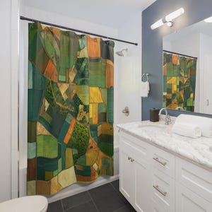 May include: A shower curtain with a colourful abstract design. The artwork features a patchwork of green, yellow, orange, and brown rectangular shapes, resembling a landscape or aerial view of fields. The curtain hangs in a bathroom with white fixtures and a dark floor.