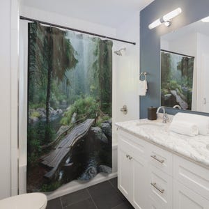 May include: A shower curtain depicting a forest scene with a wooden bridge over a river. The image shows a verdant forest with a misty atmosphere, creating a tranquil and natural ambiance for a bathroom.