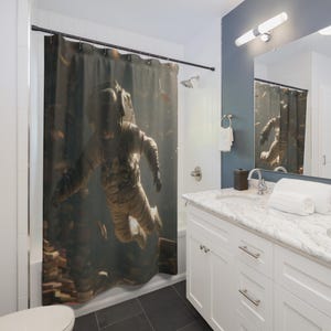 May include: A shower curtain featuring an astronaut floating in a dark, underwater environment. The astronaut is wearing a beige spacesuit. The background includes what appears to be books and other objects. The bathroom has white cabinets, a marble countertop, and a mirror.