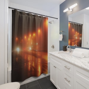 May include: A shower curtain depicting a night street scene with an orange glow from streetlights reflecting on a wet road. The image has a blurred, atmospheric effect, creating a moody ambiance.