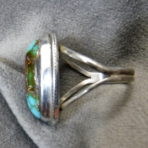 K&ouml;nnte beinhalten: Ein silberner Ring mit einem T&uuml;rkis-Stein, der in einer Zargenfassung gefasst ist. Der Ring hat ein schlichtes, elegantes Design.