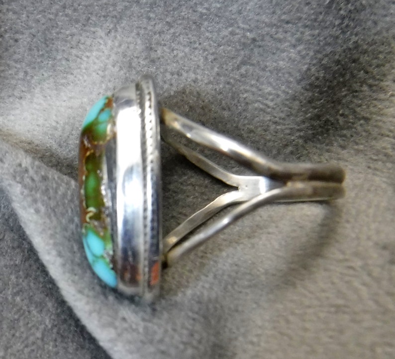 K&ouml;nnte beinhalten: Ein silberner Ring mit einem T&uuml;rkis-Stein, der in einer Zargenfassung gefasst ist. Der Ring hat ein schlichtes, elegantes Design.