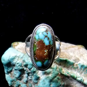 K&ouml;nnte beinhalten: Ein silberner Ring mit einem ovalen T&uuml;rkis-Stein, der in einer Zargenfassung sitzt. Der T&uuml;rkis hat eine leuchtende blaugr&uuml;ne Farbe mit brauner Matrix.