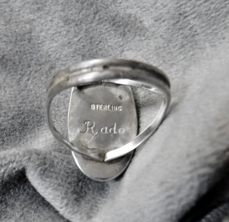 K&ouml;nnte beinhalten: Ein silberner Ring mit einem ovalen Stein. Die R&uuml;ckseite des Rings ist mit "STERLING" und "Rado" graviert.