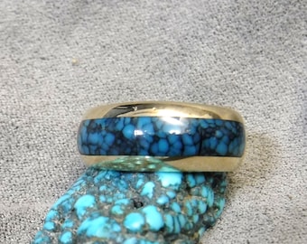 May include: A gold band ring with a blue turquoise inlay. The ring is set against a backdrop of turquoise stones.