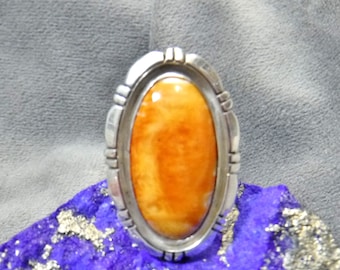 May include: A silver ring with an oval-shaped orange stone set in the center. The ring has a decorative border around the stone.