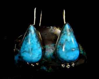 May include: A pair of silver dangle earrings featuring teardrop-shaped turquoise stones. The stones are a vibrant blue-green colour with a marbled pattern.