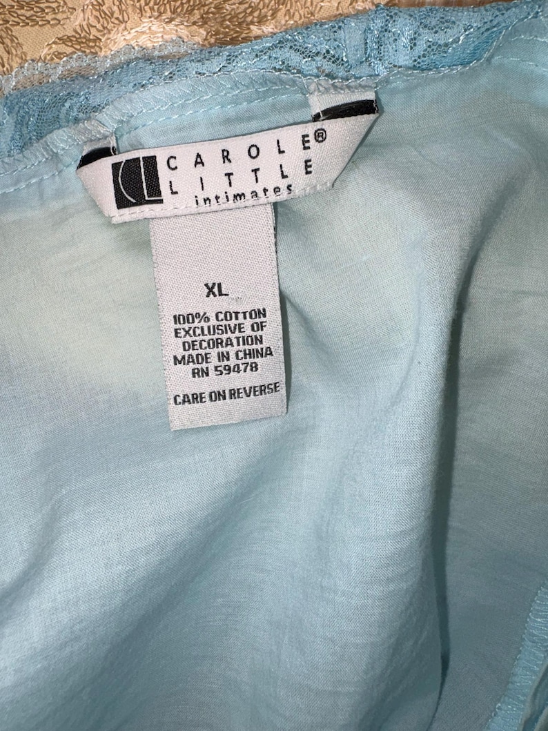 May include: A light blue garment with a lace trim. The tag reads "CAROLE LITTLE intimates" and "XL". The tag also states "100% COTTON EXCLUSIVE OF DECORATION MADE IN CHINA RN 59478 CARE ON REVERSE".