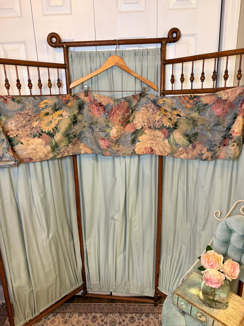 Puede incluir: Una cenefa floral vintage con fondo azul y marco de madera. La cenefa presenta grandes flores coloridas en tonos rosa, amarillo y crema. El marco es de madera oscura y tiene un dise&ntilde;o decorativo en la parte superior.
