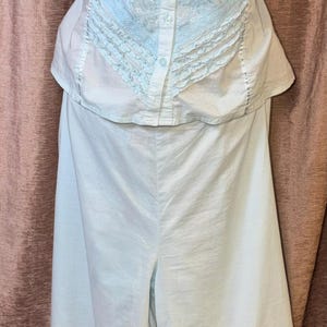 May include: A light blue and white vintage lingerie set. The top features a button-down front with lace detailing and spaghetti straps. The matching pants are wide-legged with lace trim at the hem. The set is displayed on a mannequin.