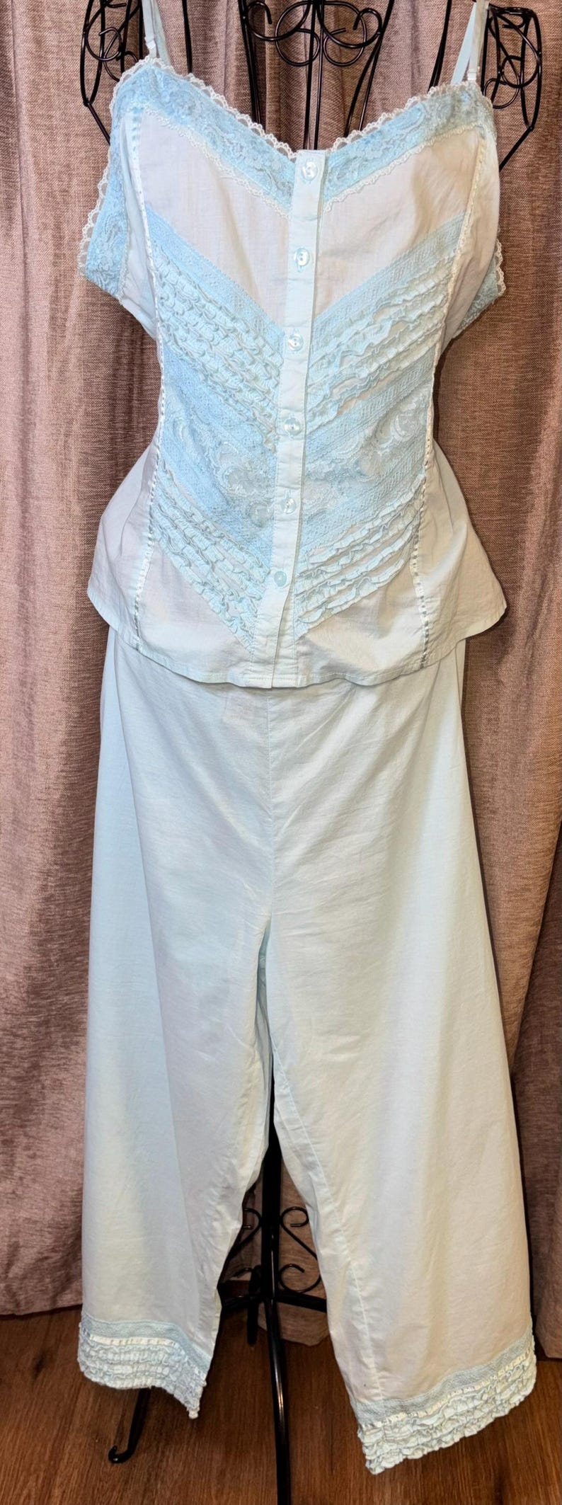 May include: A light blue and white vintage lingerie set. The top features a button-down front with lace detailing and spaghetti straps. The matching pants are wide-legged with lace trim at the hem. The set is displayed on a mannequin.