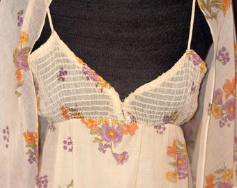 May include: A cream-colored vintage dress and matching shawl set. The dress features a V-neckline and spaghetti straps, with a floral pattern in shades of purple, orange, and yellow. The sheer shawl complements the dress, creating a cohesive ensemble.