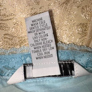 May include: A clothing care label with instructions for washing. The label is white with black text, including "MACHINE WASH COLD, GENTLE CYCLE, WASH SEPARATELY, OR WITH LIKE COLORS, ONLY NON-CHLORINE BLEACH, TUMBLE DRY LOW, COOL IRON WHEN NEEDED."