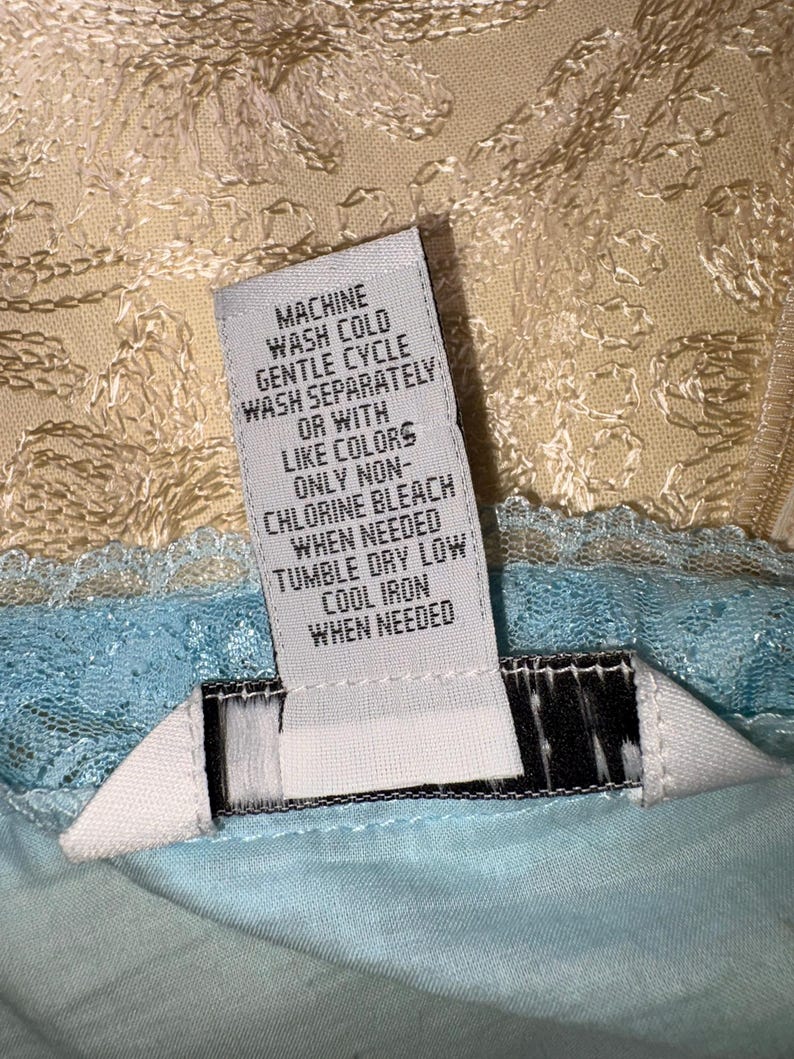 May include: A clothing care label with instructions for washing. The label is white with black text, including "MACHINE WASH COLD, GENTLE CYCLE, WASH SEPARATELY, OR WITH LIKE COLORS, ONLY NON-CHLORINE BLEACH, TUMBLE DRY LOW, COOL IRON WHEN NEEDED."