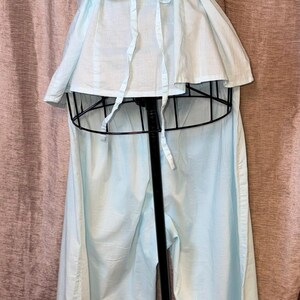 May include: A light blue vintage pajama set. The top has a peplum waist and tie closure. The camisole top has lace trim. The pajama pants are wide-legged. The set is displayed on a black mannequin.