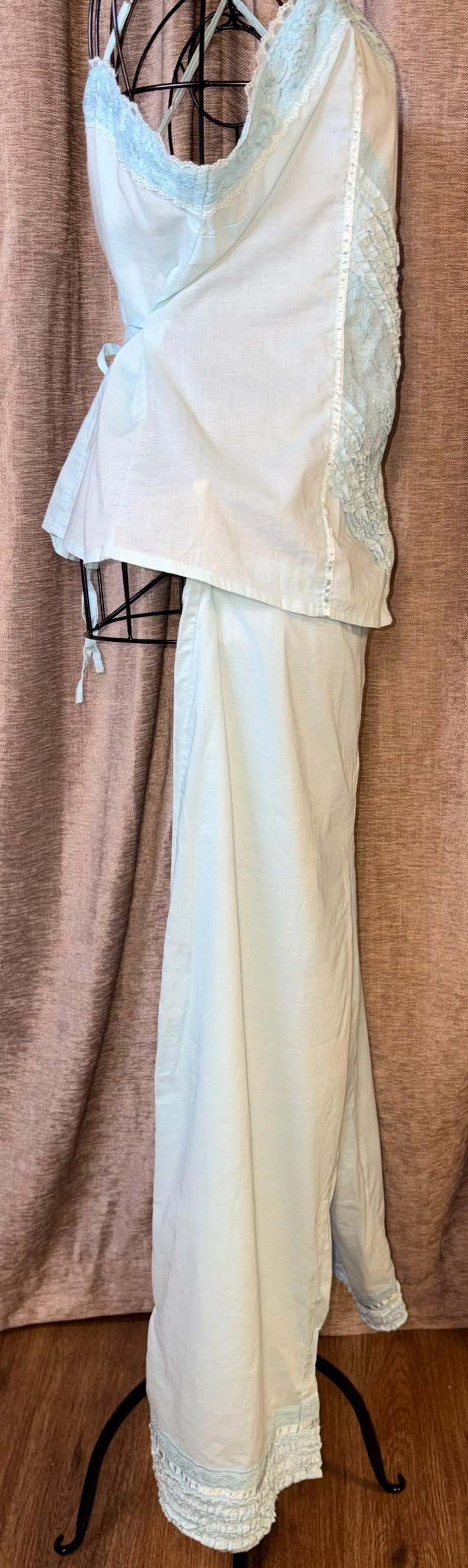 May include: A light blue vintage lingerie set, including a camisole and matching pants. The camisole features delicate lace trim along the neckline and straps. The pants have a ruffled hem. The set is displayed on a black mannequin.