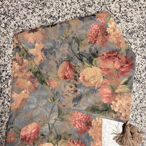 Puede incluir: Tela estampada con motivos florales en tonos azules, melocot&oacute;n y amarillo. El dise&ntilde;o presenta flores y hojas detalladas. Se adjunta una borla a juego. Ideal para la decoraci&oacute;n del hogar.