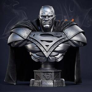 Op de afbeelding: Een metallic zilveren buste van Superman, met een strenge uitdrukking en gedetailleerde bepantsering. De buste bevat een zwarte cape en een voet met het Superman-logo. De sculptuur is een gedetailleerde weergave van de iconische superheld.