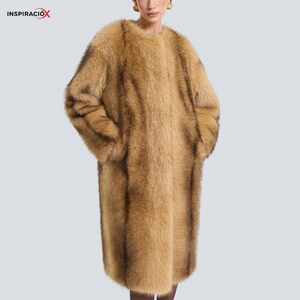 May include: A long, tan faux fur coat with a round collar. The coat has long sleeves and pockets. The coat is a solid colour with darker brown accents. The word "INSPIRACIÓX" is in the top left corner.