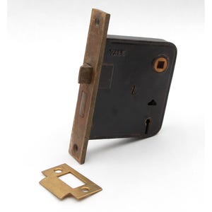 May include: Vintage Yale door lock. The lock has a black body and brass-coloured faceplate and strike plate. The lock is rectangular with a keyhole and a small square opening. The strike plate is rectangular with a central opening.