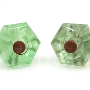 Puede incluir: Dos tiradores hexagonales de cristal verde claro con un centro marrón óxido. Los tiradores tienen un diseño facetado y están sobre un fondo blanco. Estos tiradores vintage son ideales para añadir un toque de encanto retro a los muebles.