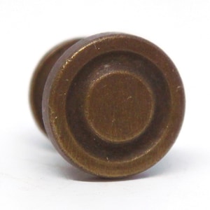 以下が含まれることがあります： 同心円のデザインが施された、丸いアンティークブラスノブ。ノブの中央はわずかに盛り上がっており、滑らかで経年変化した仕上げになっています。