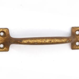 May include: A gold-toned metal door pull with a curved handle and square ends. The handle has two holes on each end.