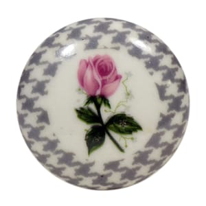 Può includere: Un pomello decorativo rotondo con un motivo floreale. Il centro presenta una rosa rosa con foglie verdi su sfondo bianco. Il bordo esterno presenta un motivo a pied-de-poule grigio e bianco. Questo pomello è probabilmente per mobili.