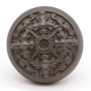 May include: A dark brown, round, decorative door knob with a detailed, intricate design of stylized leaves and flowers.