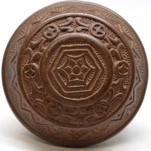 Peut inclure: Une poignée de porte ancienne en laiton ornée de motifs floraux et géométriques complexes. La poignée est de couleur brun foncé et présente une patine légèrement vieillie.