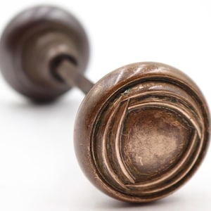 Könnte beinhalten: Antiker Türknauf aus Bronze mit kreisförmigem Design. Der Knauf hat ein detailliertes Muster und eine dunkelbraune Oberfläche. Die Hardware ist vor einem weißen Hintergrund platziert und unterstreicht ihre Vintage-Ästhetik.