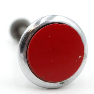 May include: A silver and red push button with a round, red center. The button is attached to a metal stem.