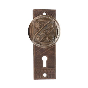 May include: A vintage brass door knob with a decorative floral pattern and a keyhole. The knob is attached to a rectangular backplate with a similar floral design.