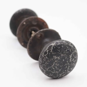 May include: Four antique, dark-colored cabinet knobs arranged diagonally on a white background. The knobs have a speckled, textured appearance, with a mix of dark gray and lighter gray tones. The knobs are likely made of metal.