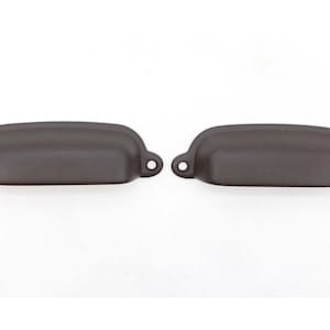 Puede incluir: Dos tiradores de armario de metal marrón con forma rectangular redondeada. Los tiradores tienen una ligera curva en el centro y están diseñados para ser utilizados en cajones o armarios.