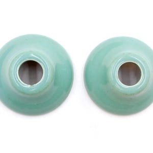 May include: Two teal ceramic candle holders with a circular opening in the center.