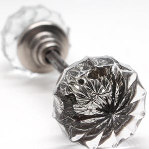 Può includere: Pomelli per porte in vetro trasparente con un design sfaccettato. I pomelli sono attaccati a un'asta di metallo e sono posti su uno sfondo bianco. Il vetro ha un aspetto decorativo di cristallo tagliato, che riflette la luce.