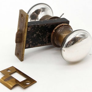 May include: A vintage brass door knob with a silver finish and a black metal backplate. The knob has a simple design and is in good condition.
