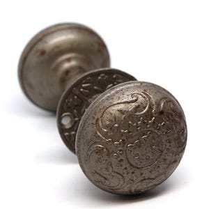 May include: Antique door knob with a decorative, ornate design. The knob is made of metal and has a worn, aged finish.