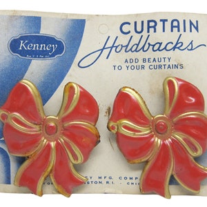 May include: A pair of red and gold bow-shaped curtain holdbacks on a white card with the text "CURTAIN Holdbacks ADD BEAUTY TO YOUR CURTAINS" and "Kenney MFG. COMP.  STON. R.I.  CHIC".