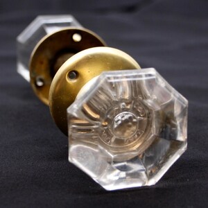 May include: A vintage glass door knob with an octagonal shape and a brass backplate. The knob has a raised design and the words "S. & J.  CO.  PAT.  APR.  18,  1882" are etched into the glass.