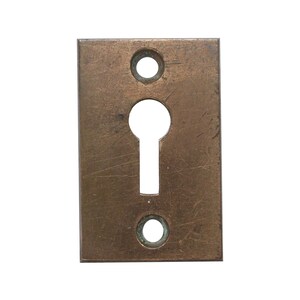 May include: A rectangular keyhole cover made of brass with a worn, aged finish. The cover has two small round holes on either side of the keyhole.