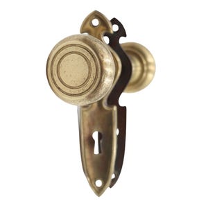 Peut inclure: Ensemble de poignée de porte en laiton antique avec trou de serrure. Le bouton est rond avec des cercles concentriques. La plaque arrière est ornée d'un motif décoratif. L'ensemble est en laiton et a un aspect vintage.