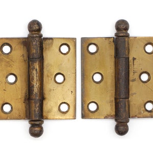 May include: Two antique brass hinges with rounded finials. The hinges are closed and have a worn, aged look.