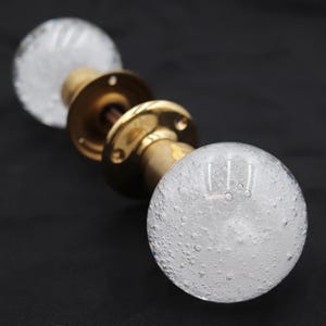 May include: A pair of vintage door knobs featuring clear, bubble-textured glass spheres and brass fittings. The knobs are mounted on a brass rod with decorative plates. The glass spheres have a unique, textured appearance.